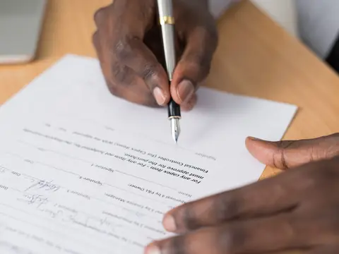 A close view of two hands signing a printed document with a pen on a light wood table